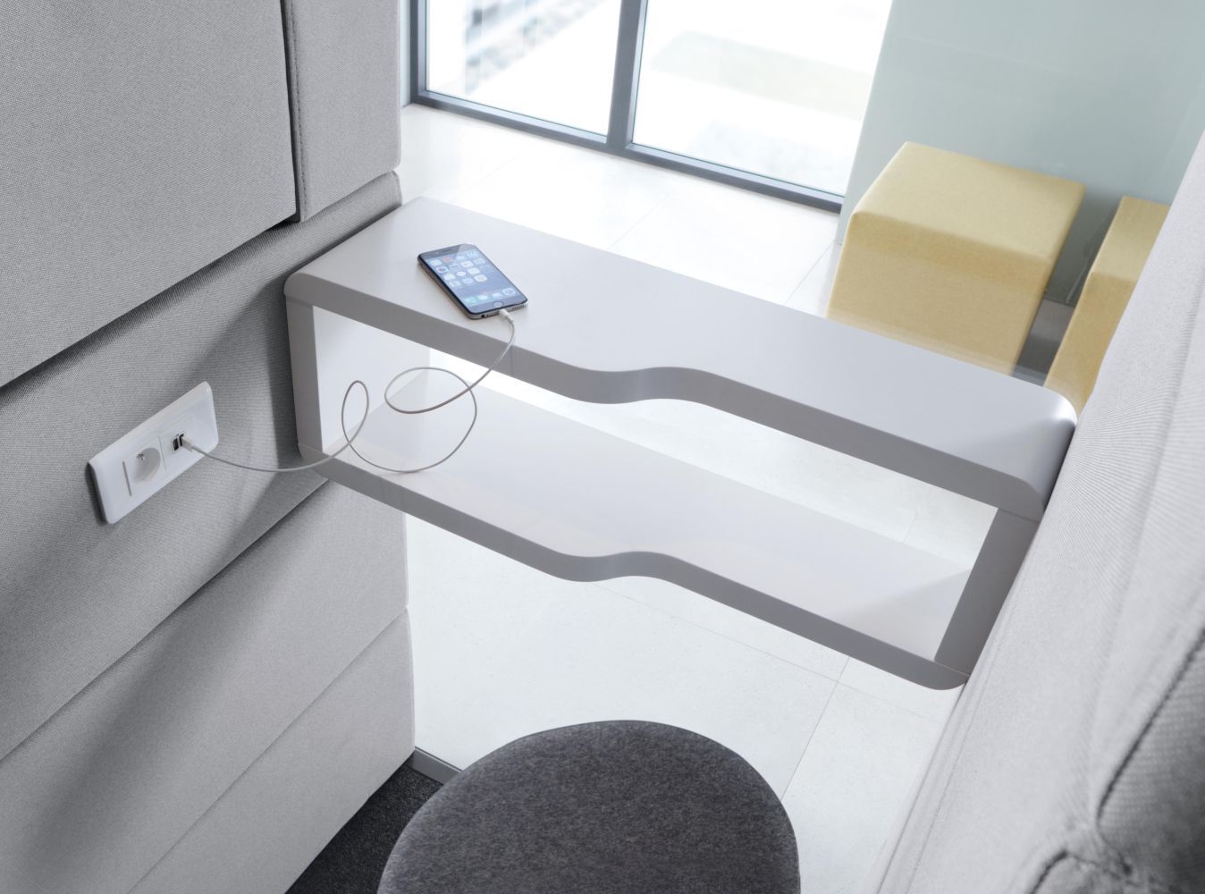 Smartphone lädt auf modernem, ergonomischem Tisch mit integriertem USB-Anschluss in grauer Büroumgebung.