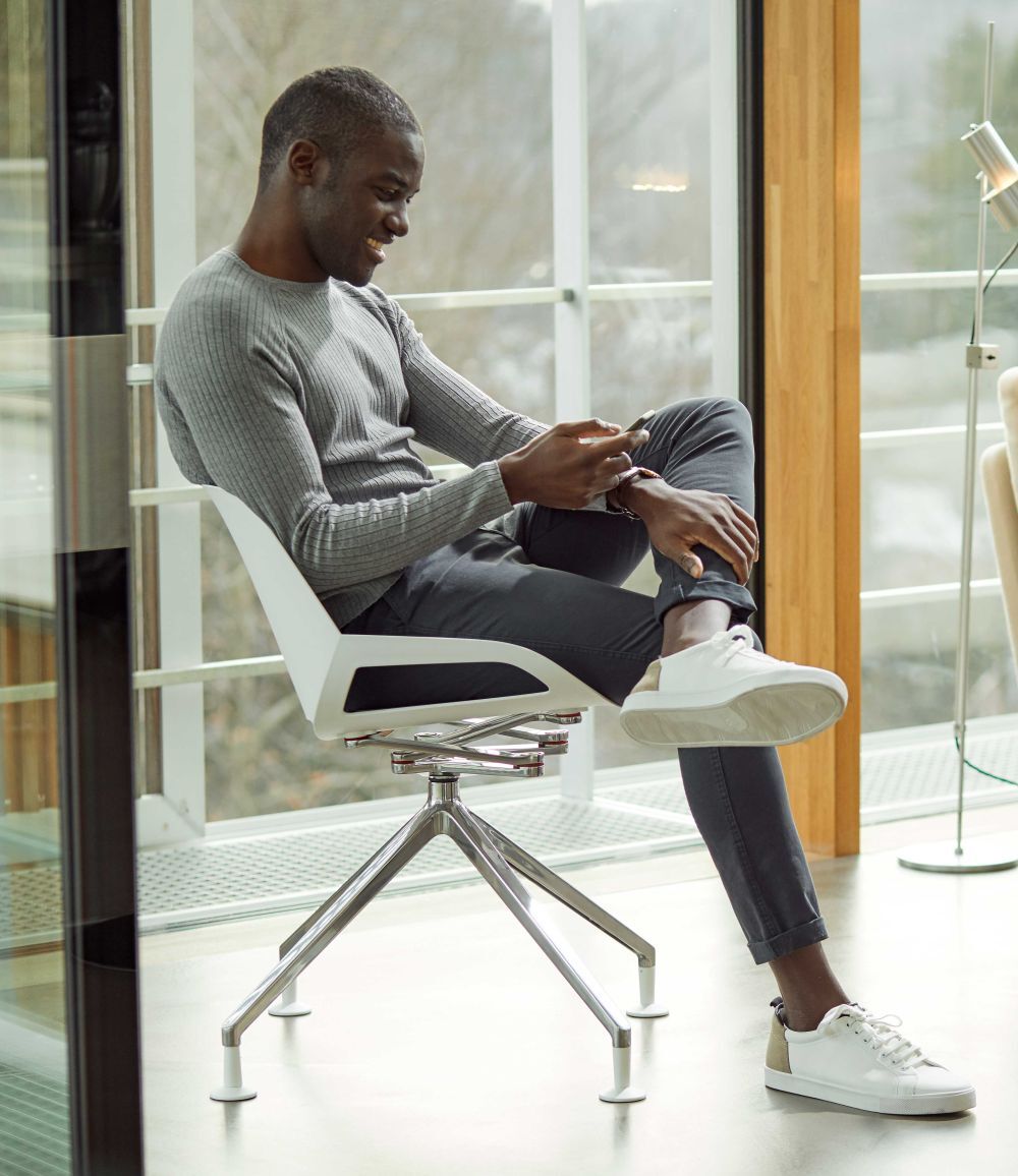 Mann sitzt entspannt auf einem ergonomischen Stuhl mit Smartphone in modernem, lichtdurchflutetem Raum.