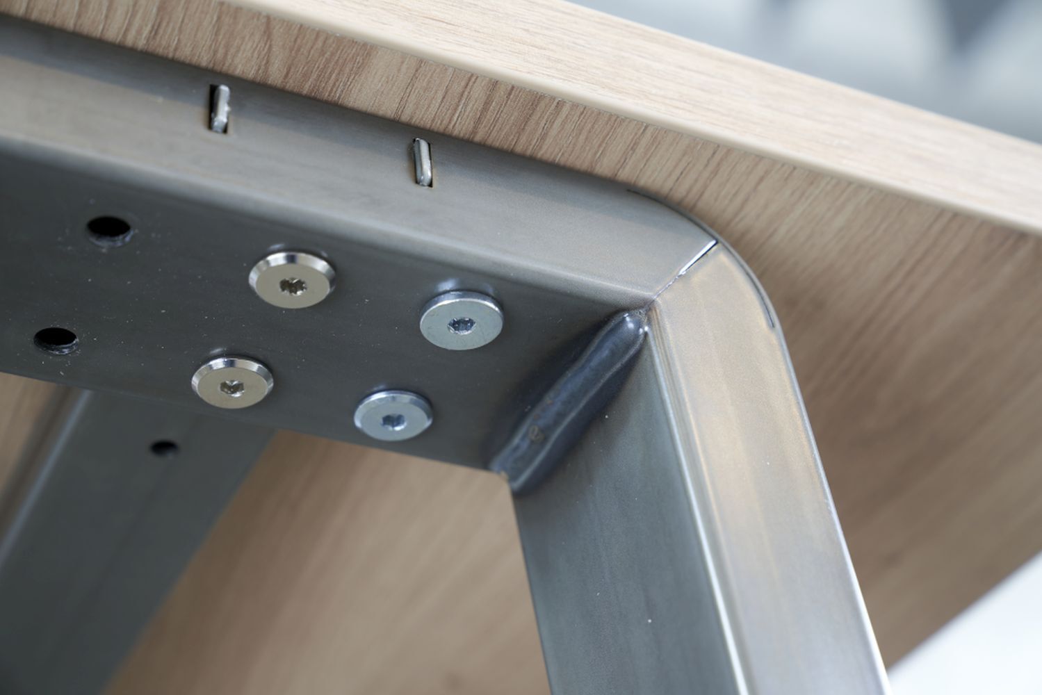 Detailansicht einer robusten Stahlrahmenverbindung unter einem Holztisch, zeigt Verschraubungen und hochwertige Verarbeitung.