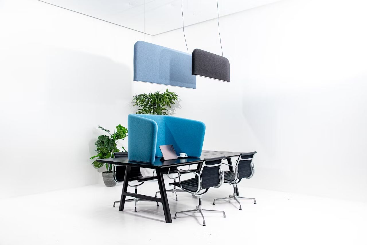 Moderner Konferenztisch mit vier ergonomischen Stühlen, blauen Trennwänden und Pflanzen in minimalistischem Bürodesign.