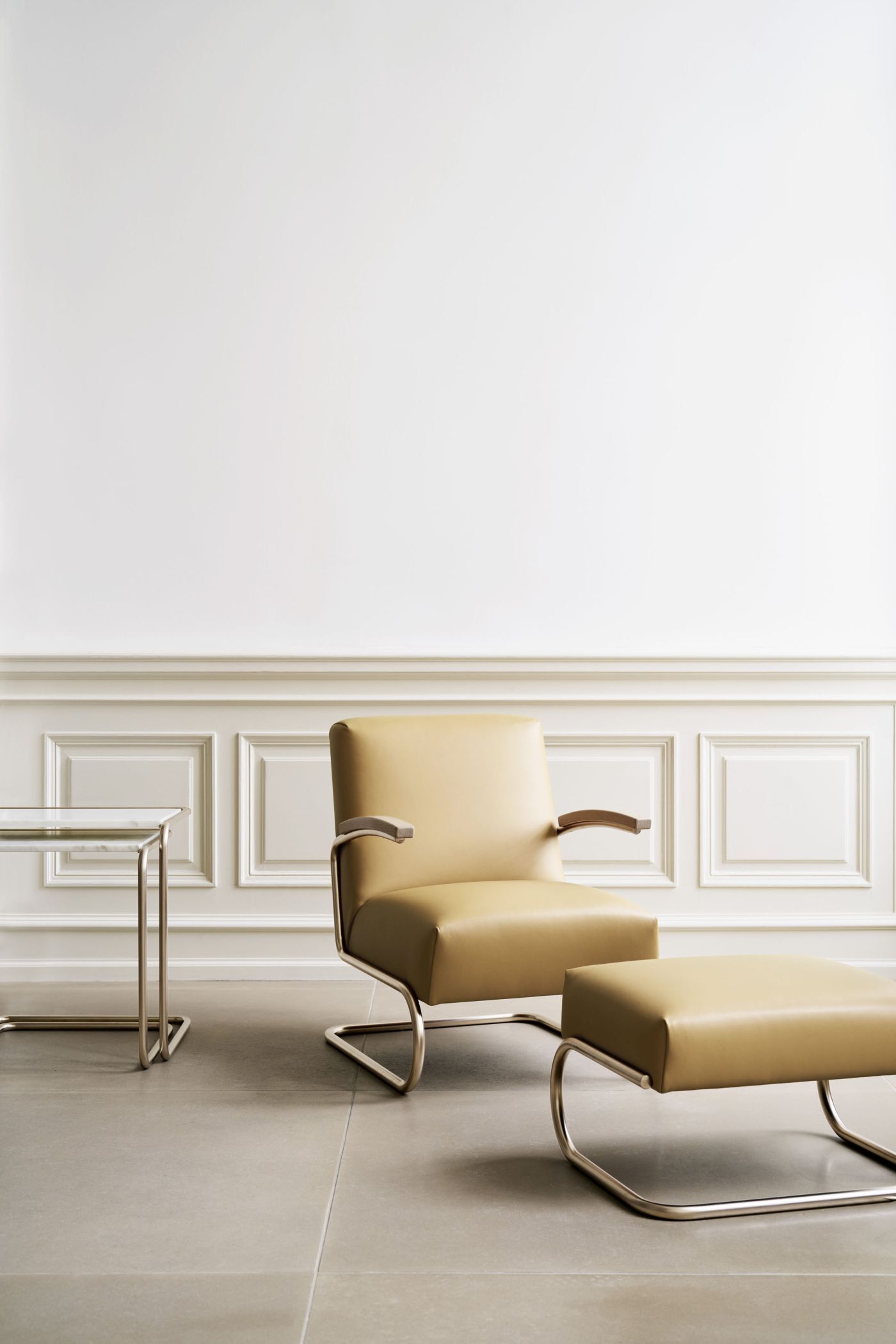 Eleganter Ledersessel mit passendem Hocker und Tisch vor klassischer weißer Wandverkleidung.