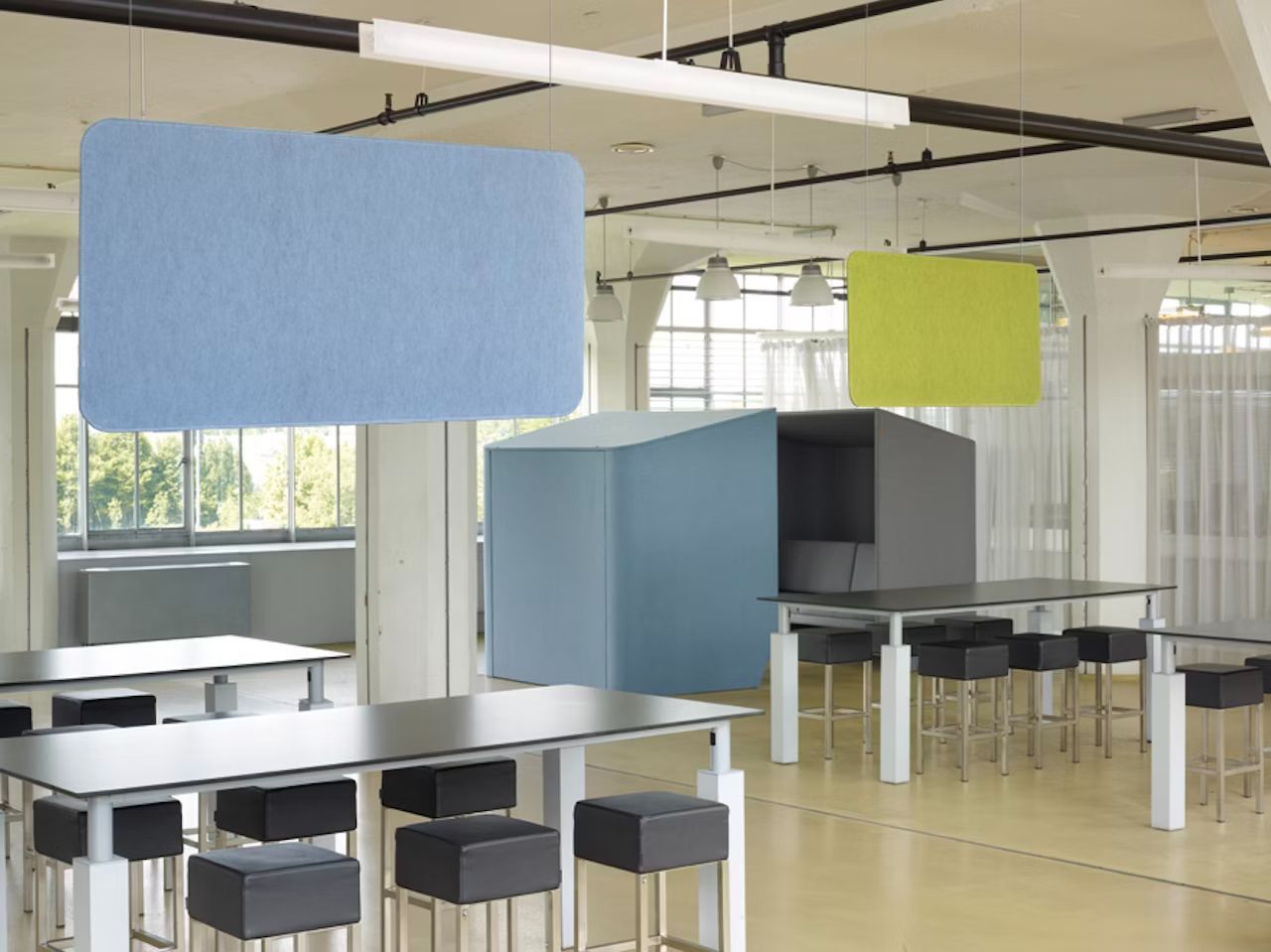 Moderne Büroumgebung mit ergonomischen Stühlen, hohen Tischen und hellen Akustikpaneelen an der Decke.