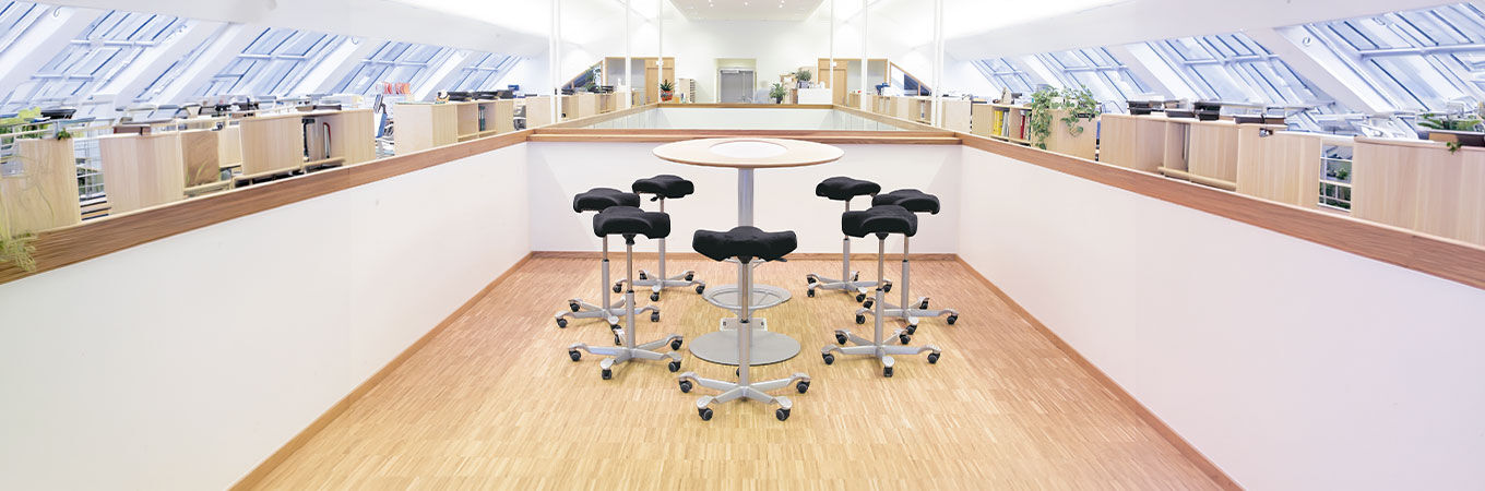 Sechs ergonomische Sitzhocker um einen runden Tisch, ideale Lösung für bewegtes Sitzen im Büro.