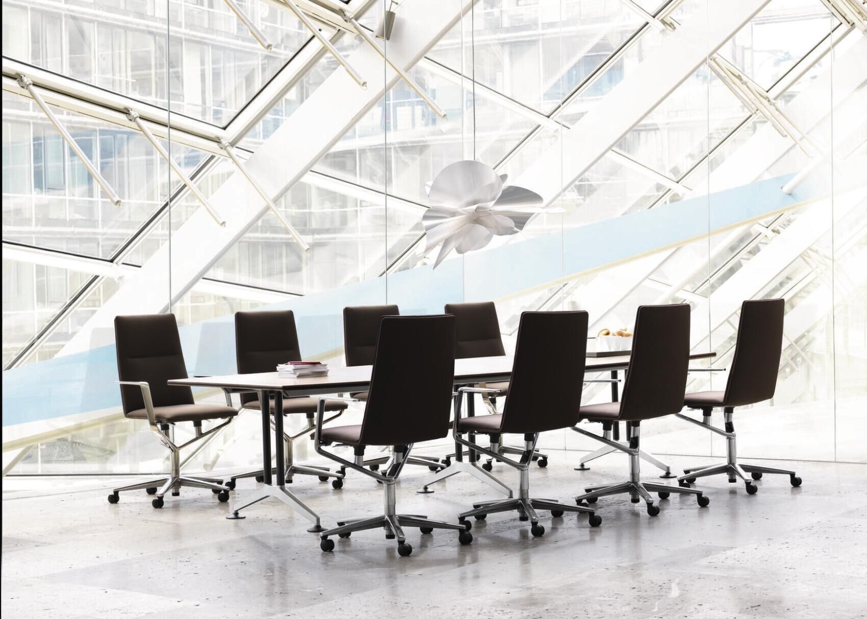 Moderner Konferenzraum mit ergonomischen Bürostühlen an einem langen Tisch vor großen Glasfenstern.