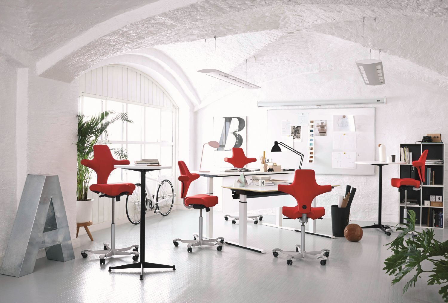 Moderner Büroraum mit roten ergonomischen Bürostühlen, weißen Tischen, Fahrrad und Pflanzen unter gewölbter Decke.