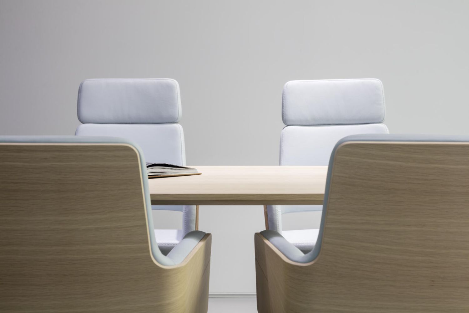 Vier elegante, ergonomische Bürostühle aus Holz und Leder um einen modernen Konferenztisch.