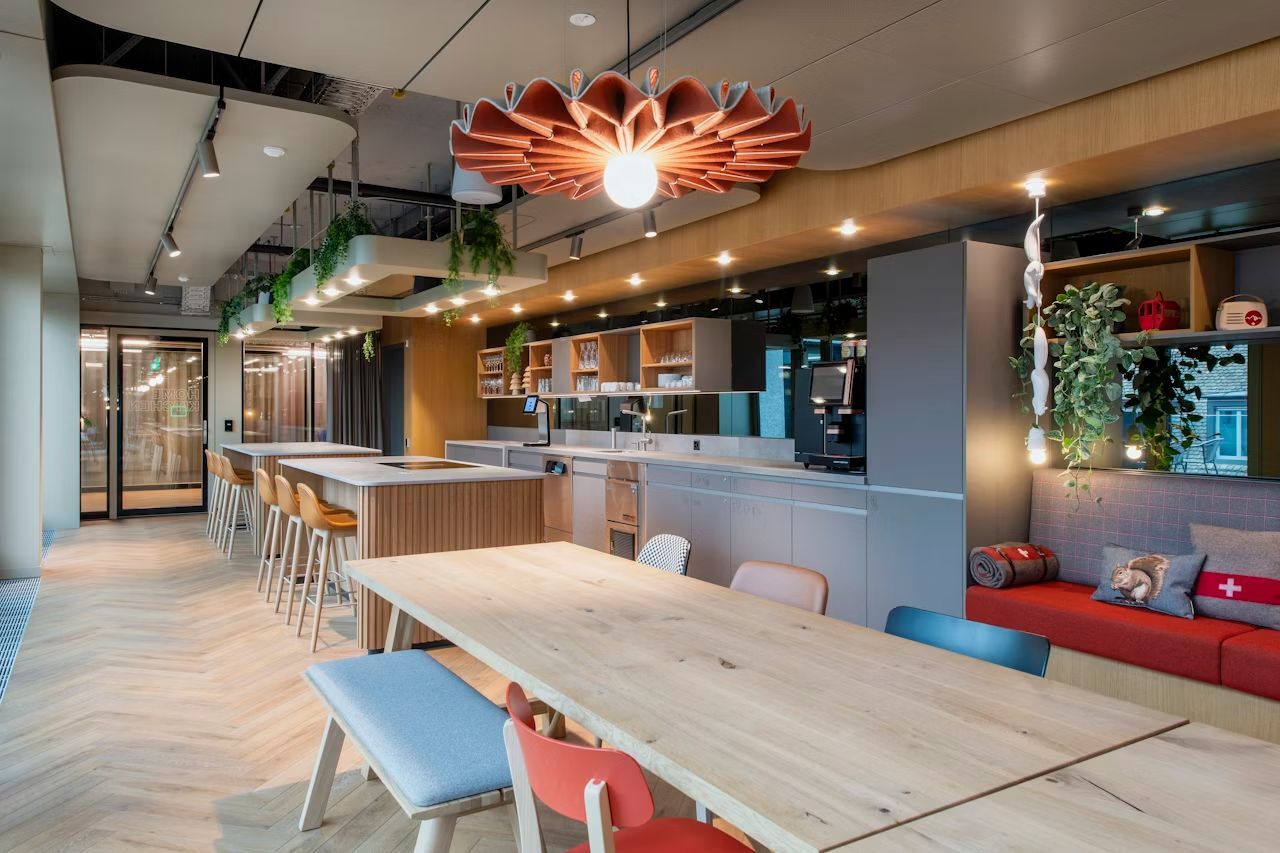 Moderne Büroküche mit Holzdekor, hängenden Pflanzen und ergonomischen Sitzmöbeln, strahlt eine einladende Atmosphäre aus.