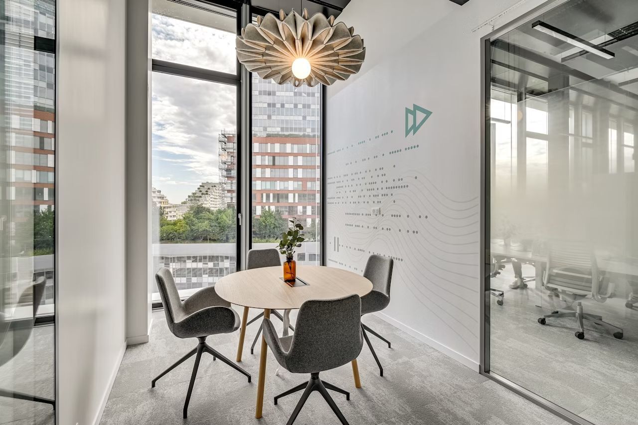Moderner Besprechungsraum mit vier ergonomischen Stühlen um einen runden Tisch, große Fenster mit Stadtblick.