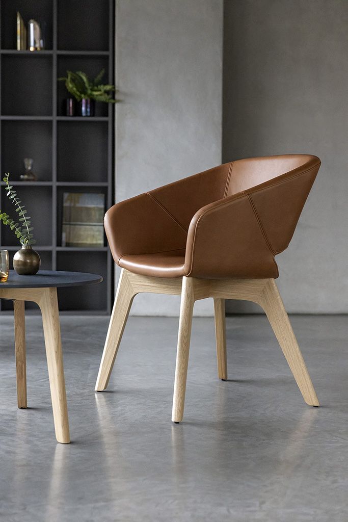Ergonomischer Bürostuhl mit braunem Lederbezug und Holzbeinen, neben einem Tisch in modernem Raum.
