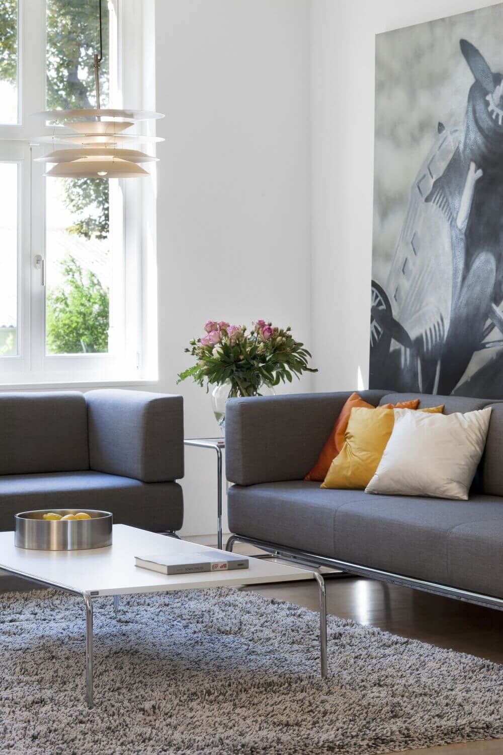Moderner Wohnraum mit grauen Sofas, Couchtisch, Blumenvase und großem Kunstwerk im Hintergrund.