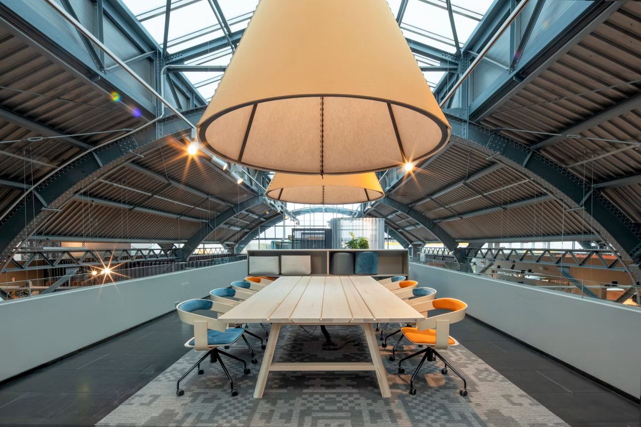 Moderner Tagungsraum mit ergonomischen Stühlen und großem Holztisch unter einem Gewölbedach.