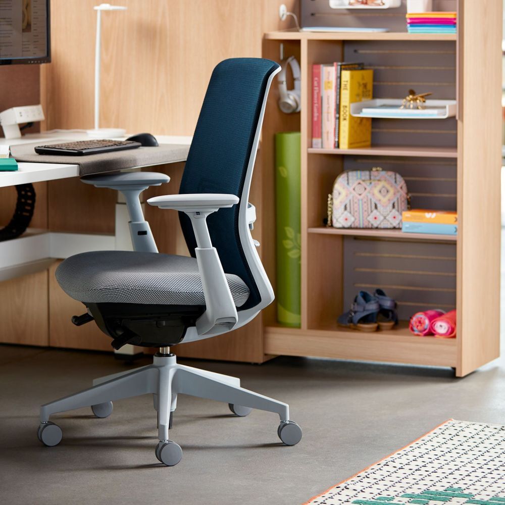 Ein ergonomischer Bürostuhl vor einem Schreibtisch in einem modernen Arbeitsbereich mit Regalen im Hintergrund.
