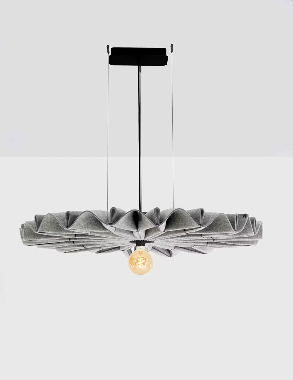 Moderne, hängende Designerlampe mit gefaltetem grauem Schirm und sichtbarer Glühbirne in schlichter Umgebung.