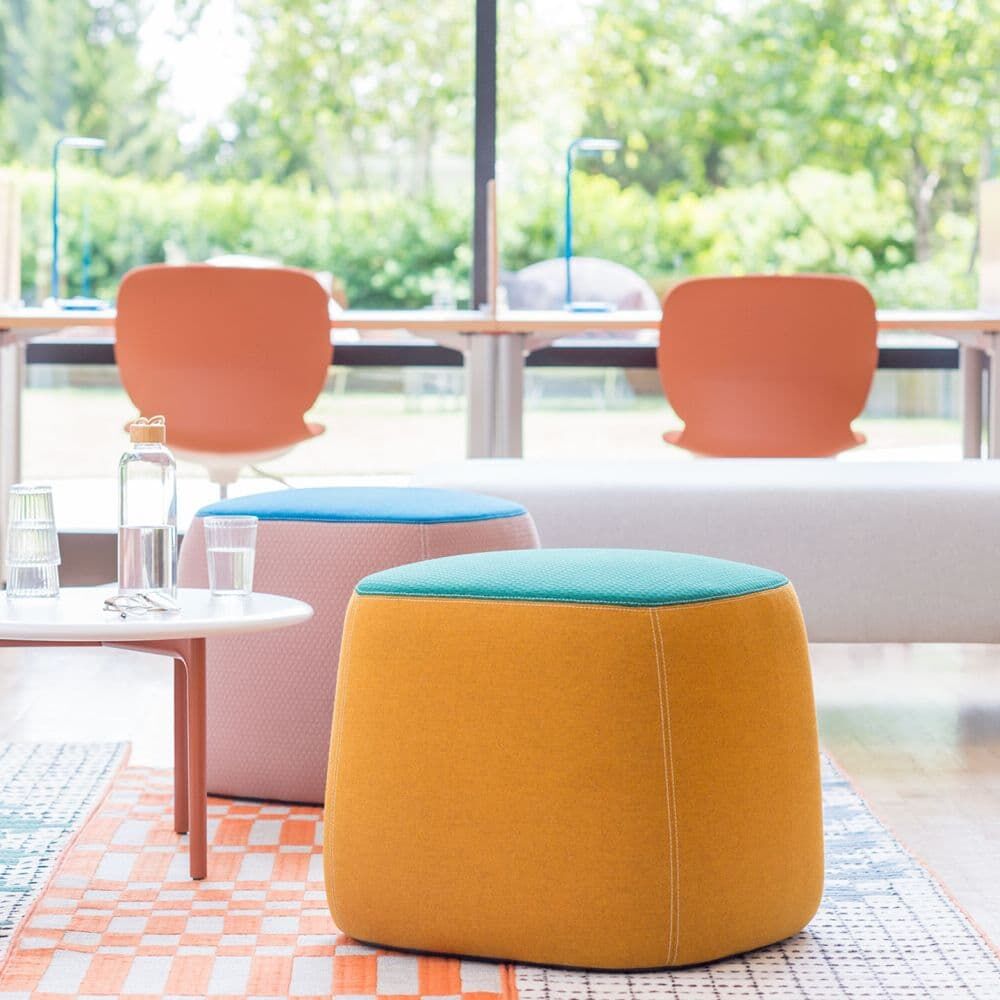 Bunte ergonomische Hocker in modernem Büro mit großen Fenstern und Schreibtischen im Hintergrund.
