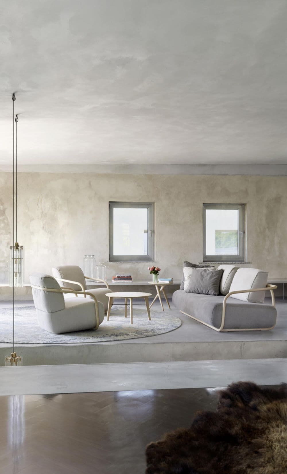 Moderne Lounge mit ergonomischen Sesseln und Sofa, Holztisch und Hängelampe in heller, minimalistischer Umgebung.