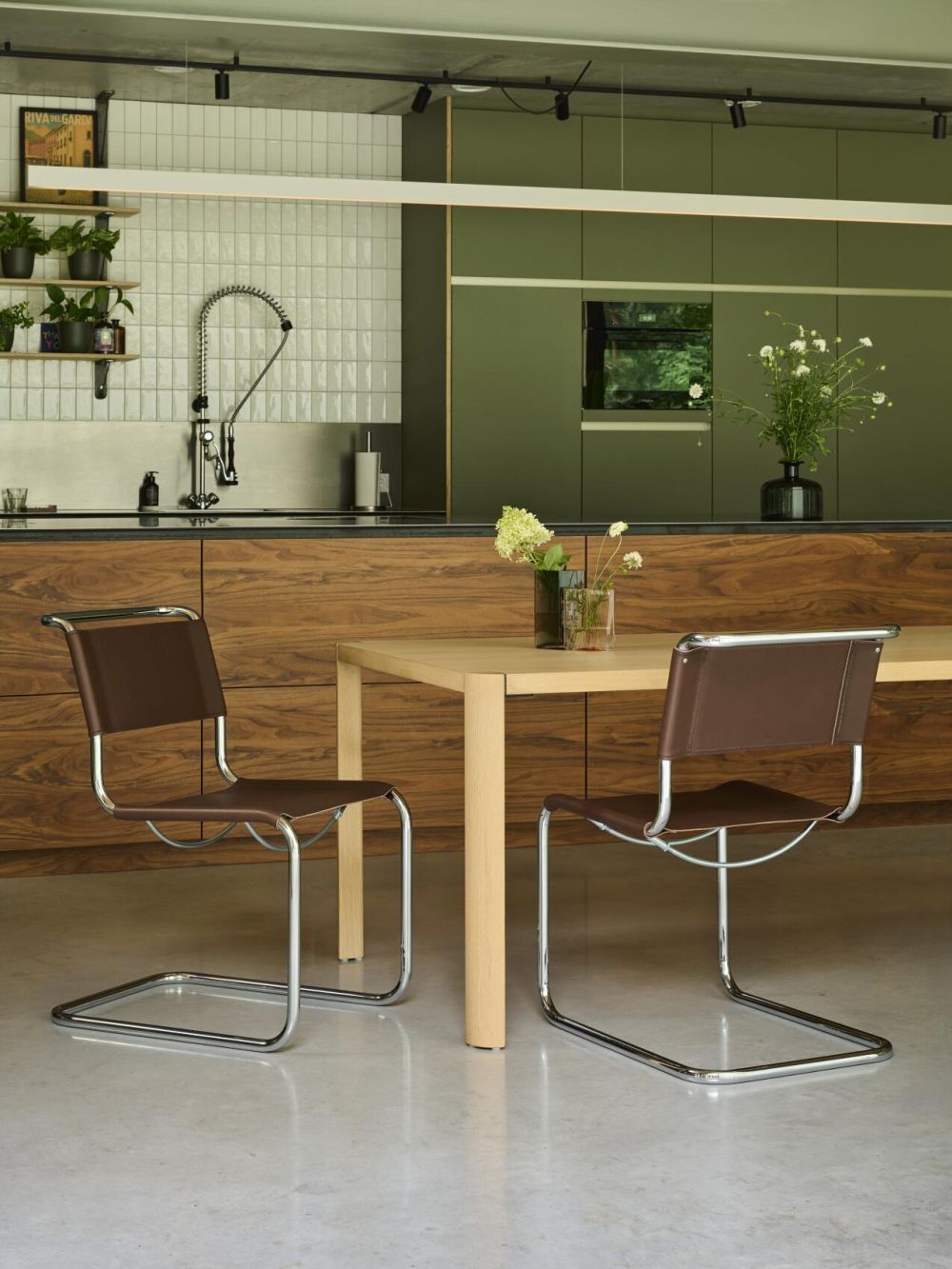Moderner Esstisch mit zwei braunen Freischwingerstühlen in einer stilvollen Küche mit grünen Schränken und Blumen.