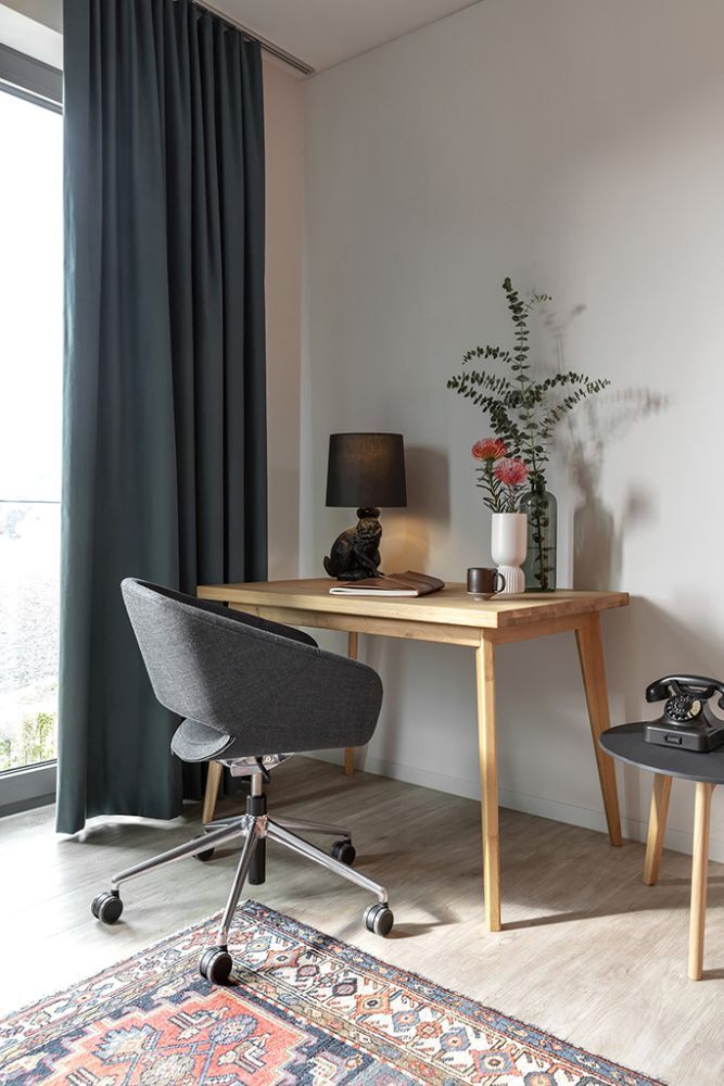 Moderner Arbeitsplatz mit ergonomischem Drehstuhl, Holztisch, Tischlampe und dekorativen Pflanzen in hellem Raum.