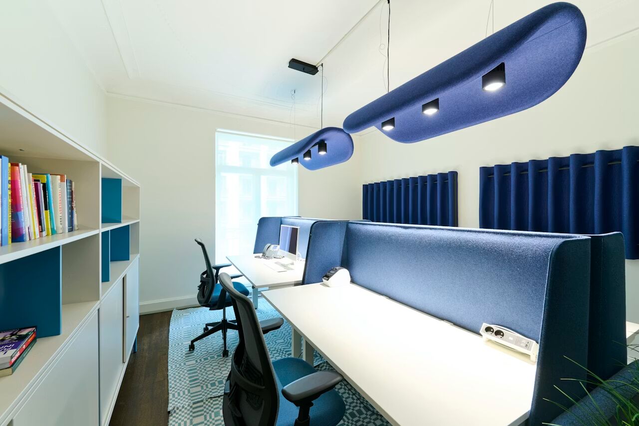 Modernes Büro mit ergonomischen Stühlen und blauen Trennwänden, Akustikpaneelen und hängenden Lampen.