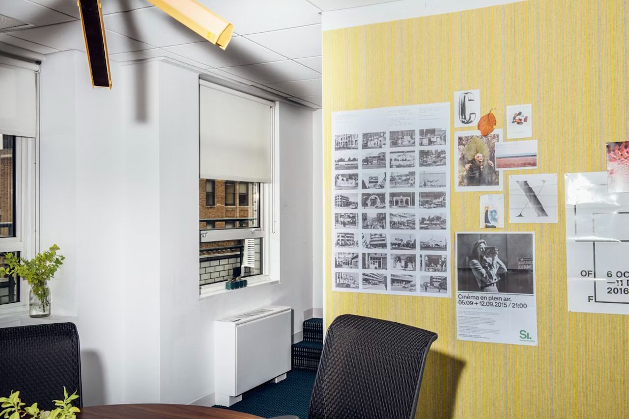 Büro mit ergonomischem Stuhl, Fenster und inspirierender Pinnwand mit Fotos und Postern an gelber Wand.