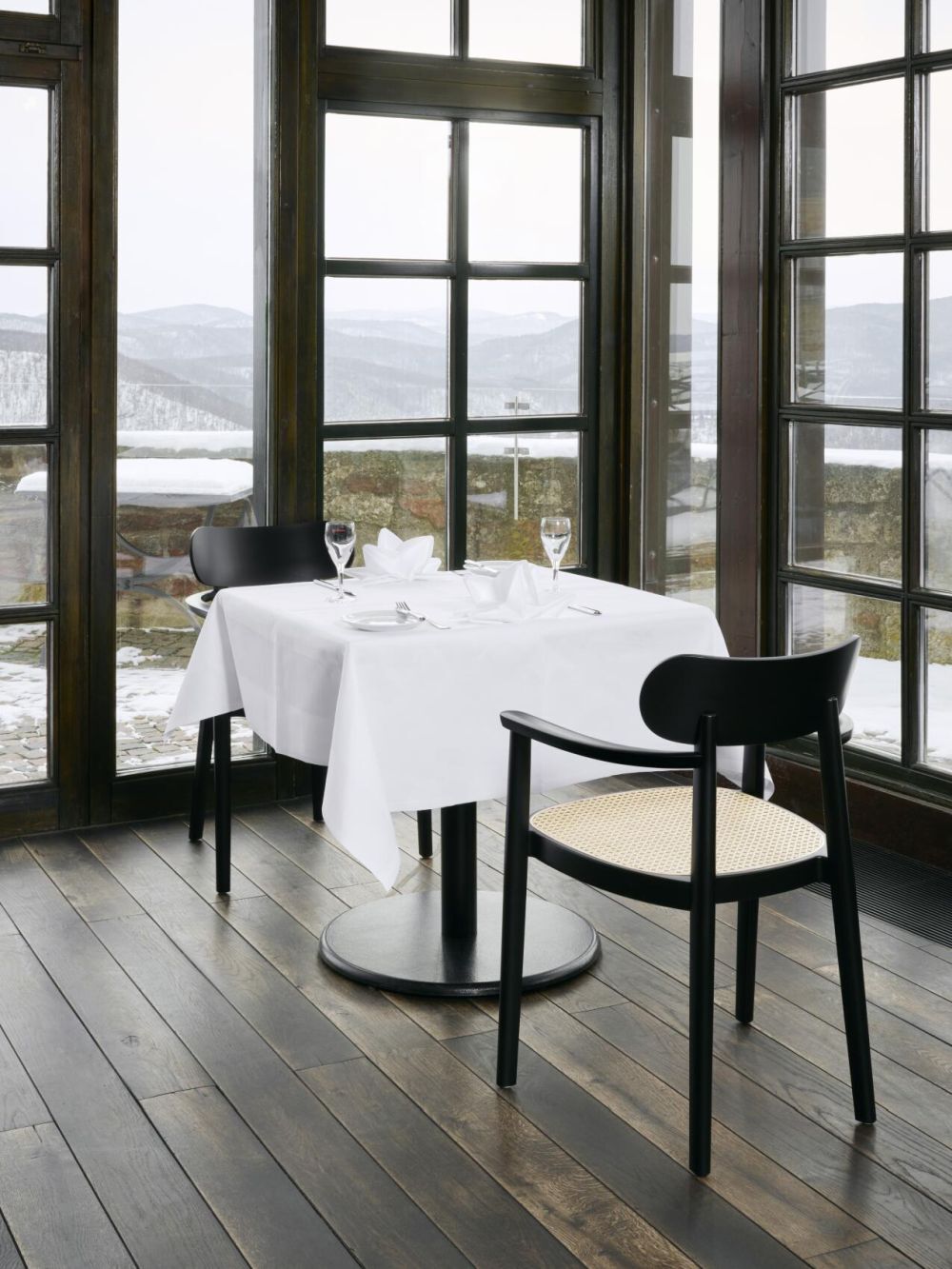 Elegantes Esszimmer mit zwei schwarzen Stühlen am gedeckten Tisch, mit Aussicht auf verschneite Berge.