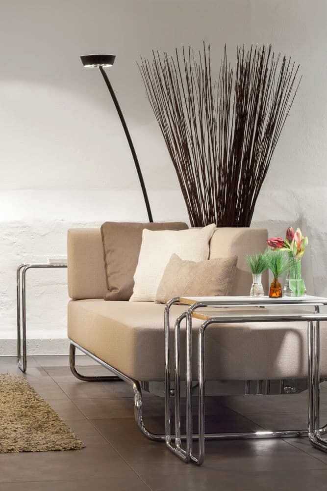 Moderne, beige Couch mit Kissen, neben einem eleganten Stehlampe und stilvollen Beistelltischen mit Dekorationen.