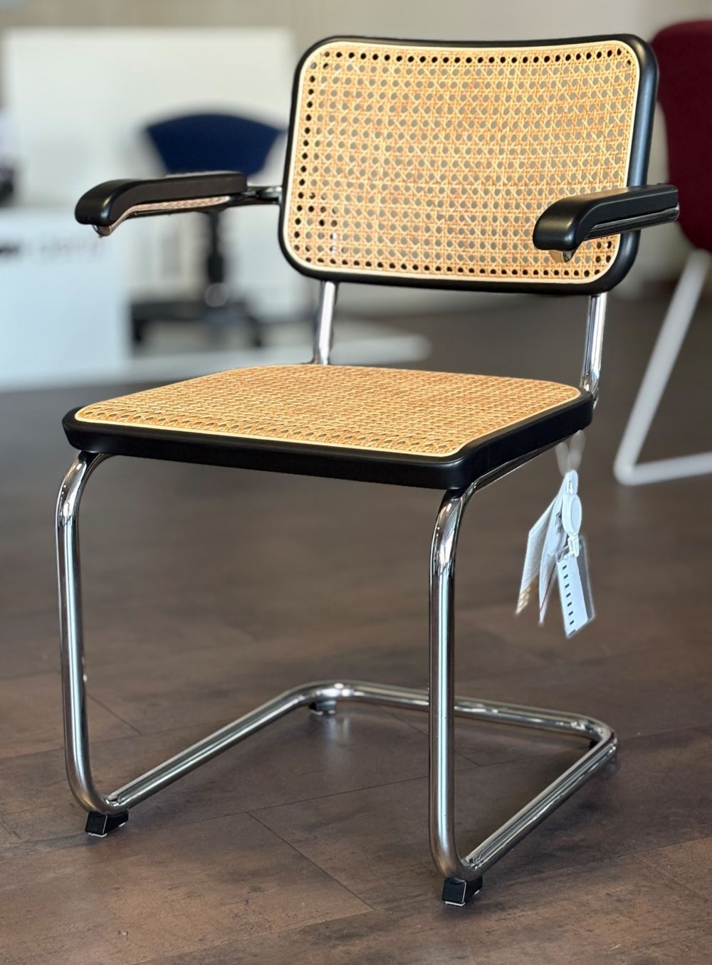 Zeitgenössischer Freischwinger mit Geflecht-Sitzfläche und verchromtem Gestell auf Holzboden in modernem Büroausstellungsraum.