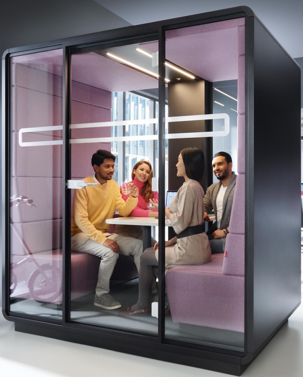 Vier Personen in einer modernen, schallisolierten Besprechungskabine mit Glaswänden, die in einem Bürogebäude sitzen.