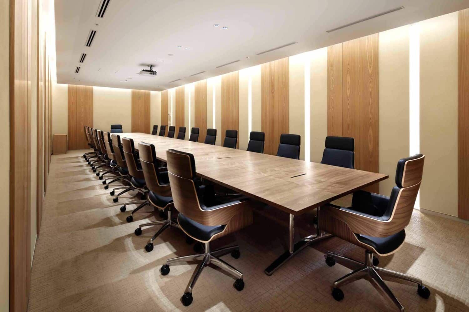 Großer Konferenzraum mit langem Holztisch, umgeben von ergonomischen schwarzen und braunen Bürostühlen.