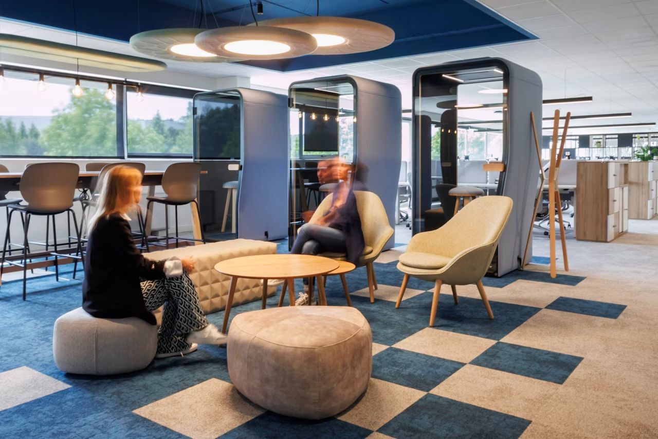Moderne Büroumgebung mit ergonomischen Möbeln, besetzt mit Personen und schallisolierten Kabinen im Hintergrund.