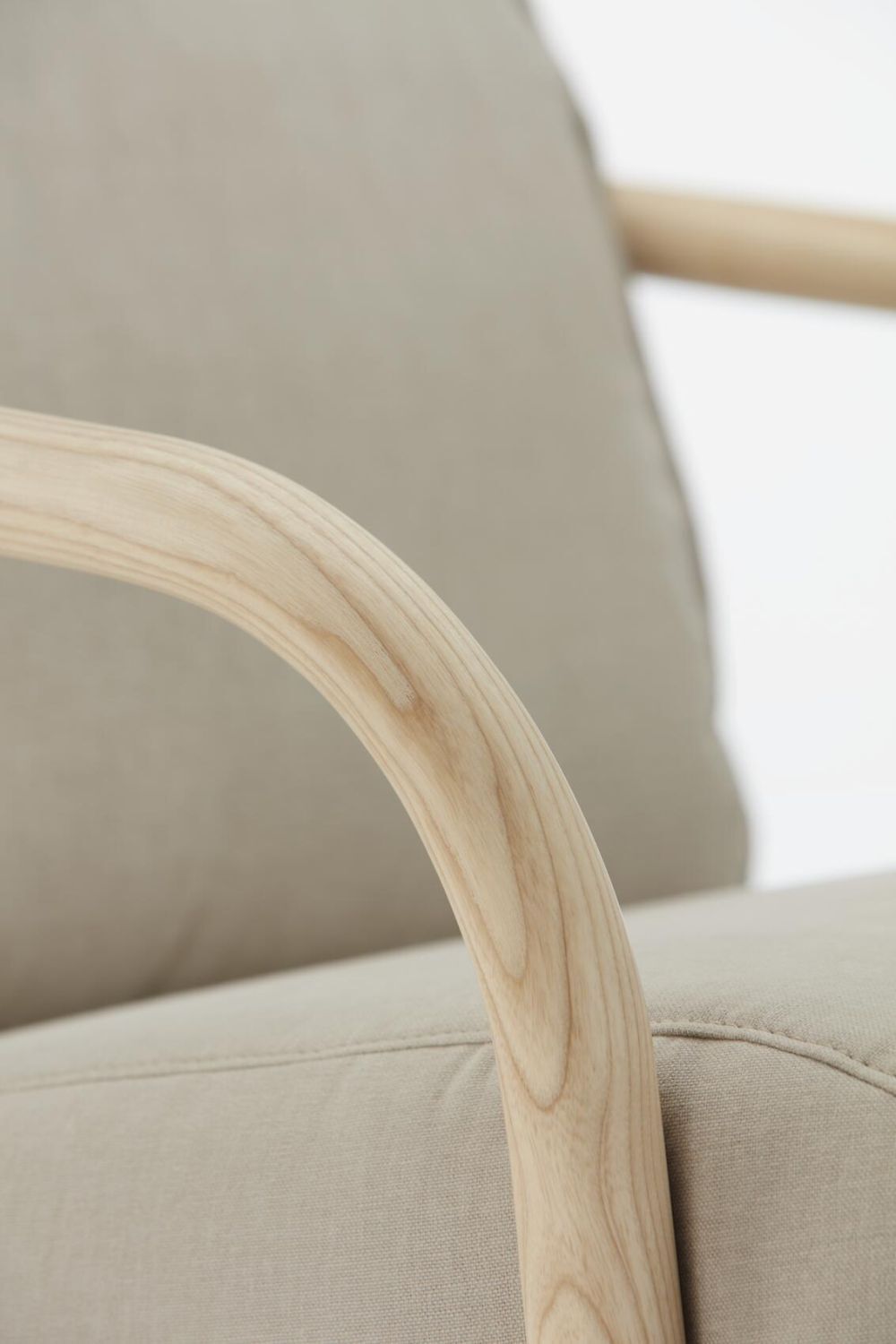 Nahaufnahme eines ergonomischen Stuhlarmlehne aus hellem Holz vor beigem Stoffbezug.