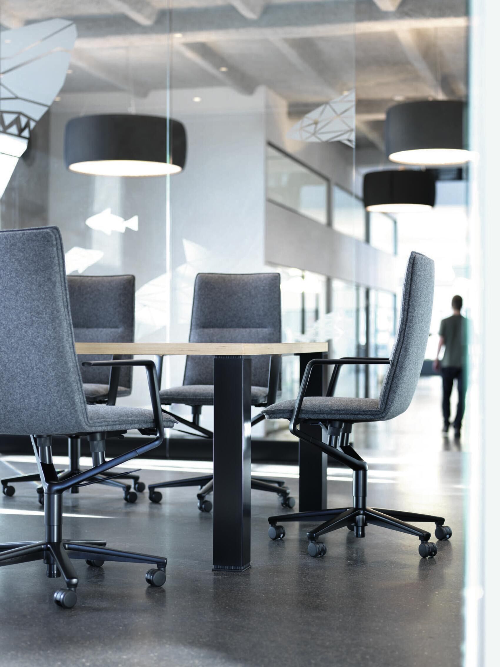 Moderner Konferenzraum mit grauen ergonomischen Stühlen und einem runden Holztisch, im Hintergrund Glaswände.
