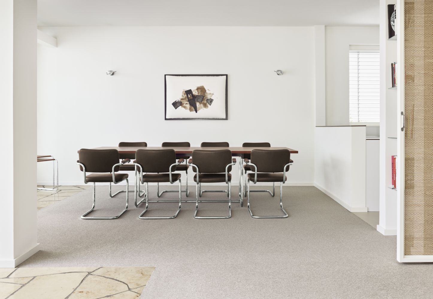 Minimalistischer Konferenzraum mit moderner Kunst an der Wand und acht ergonomischen Stühlen um einen Tisch.