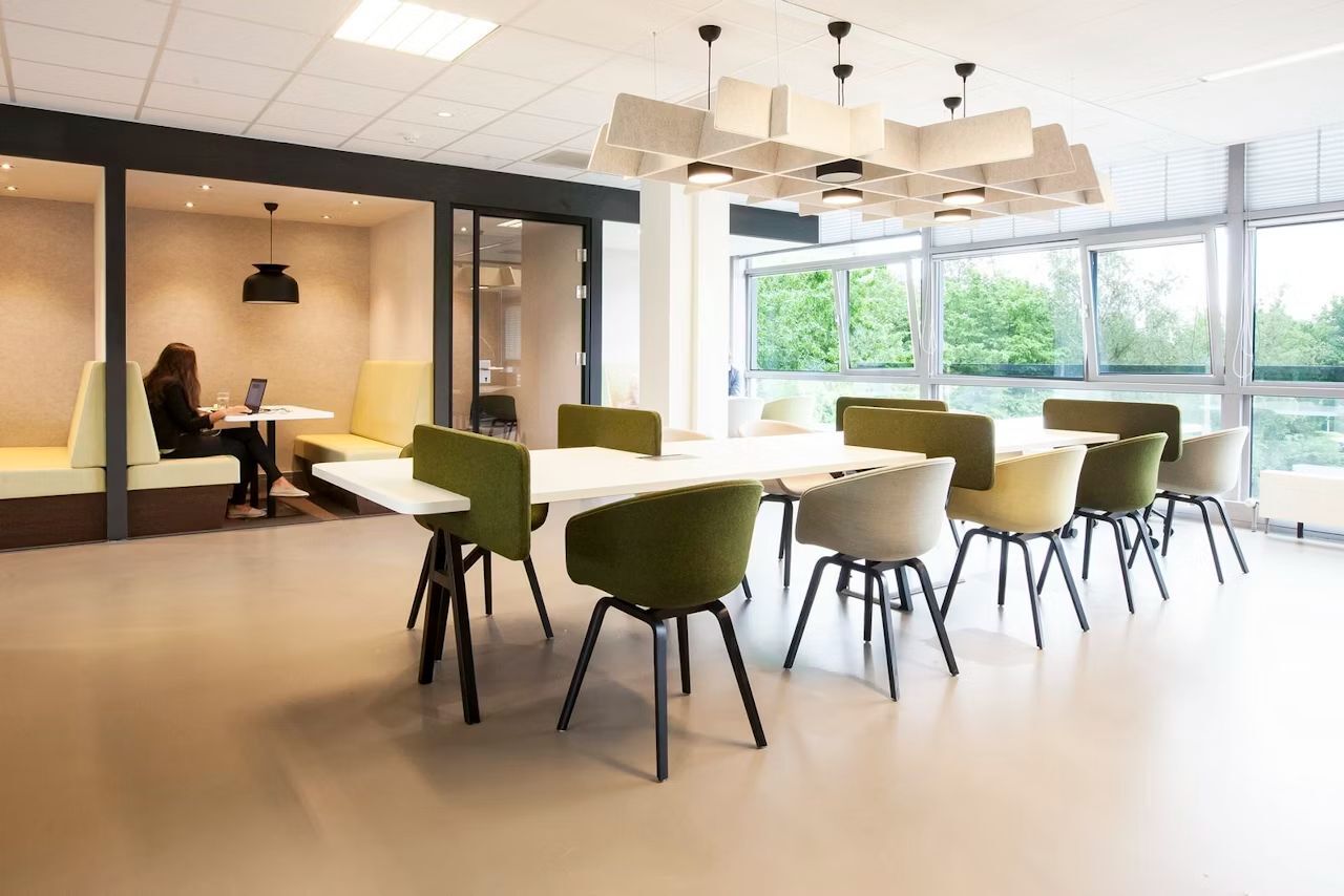 Moderne Büroeinrichtung mit ergonomischen Stühlen und Schreibtischen, helle Fenster, Person arbeitet in Nische.