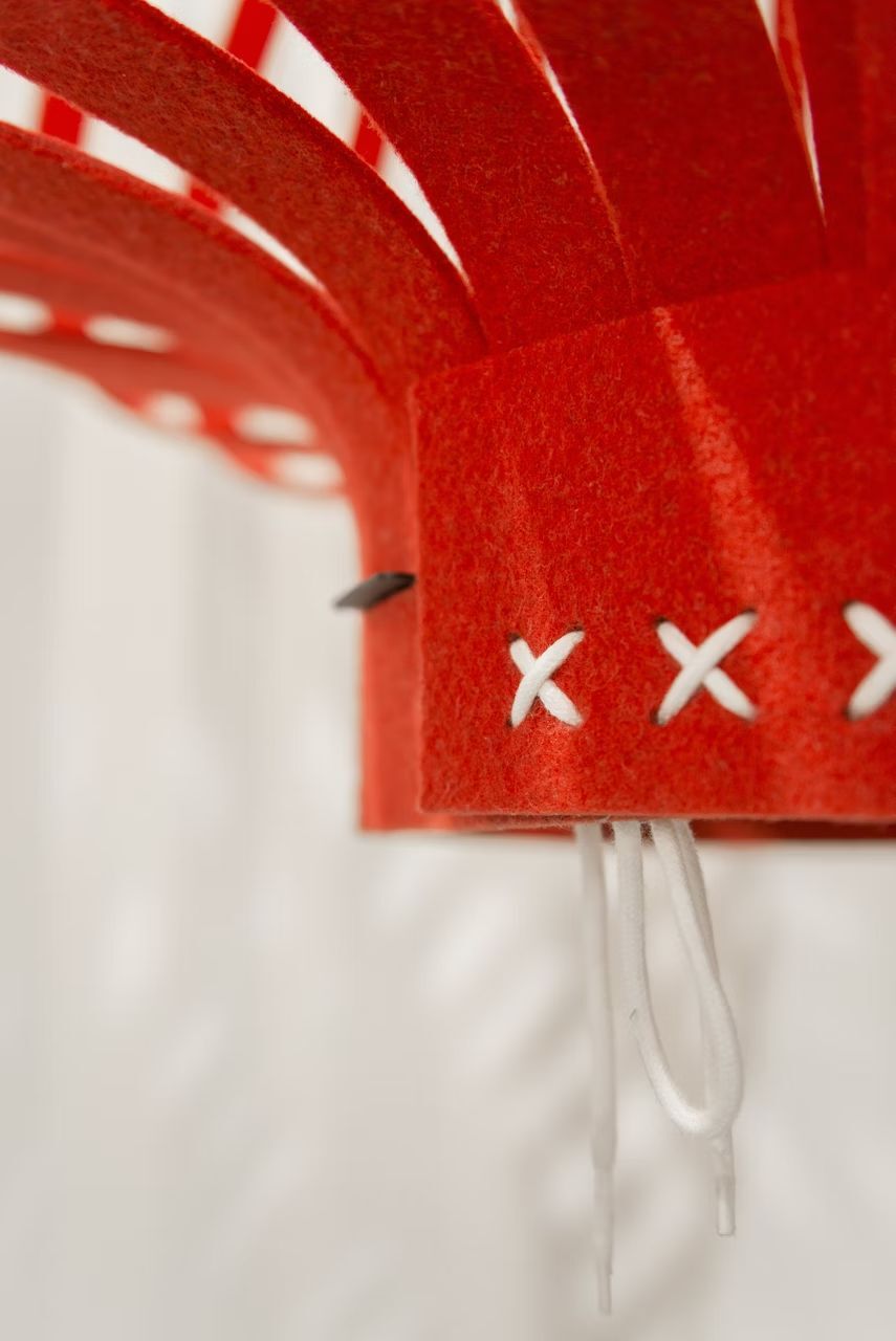 Nahaufnahme einer roten, filzartigen Struktur mit weißen Kreuzstichen und Lichtspiel im Hintergrund.