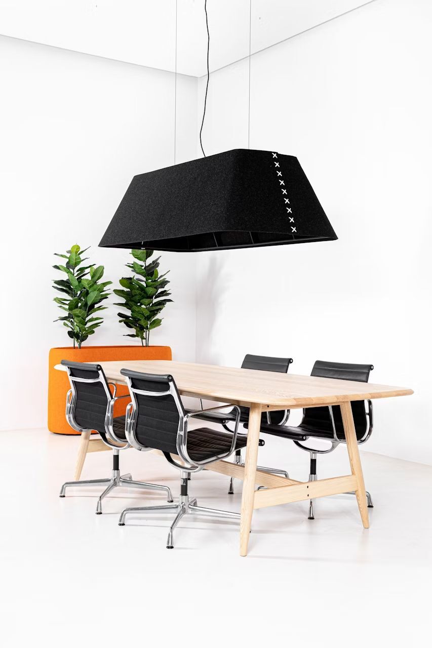 Moderner Konferenztisch mit vier ergonomischen Stühlen, zwei Pflanzen und einer schwarzen, rechteckigen Hängelampe.