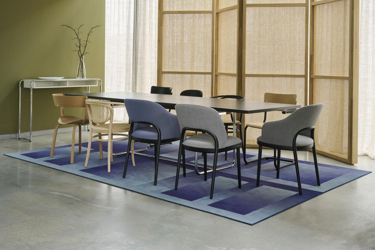 Moderne Besprechungsecke mit verschiedenen ergonomischen Stühlen um einen rechteckigen Tisch, auf blauem Teppich.