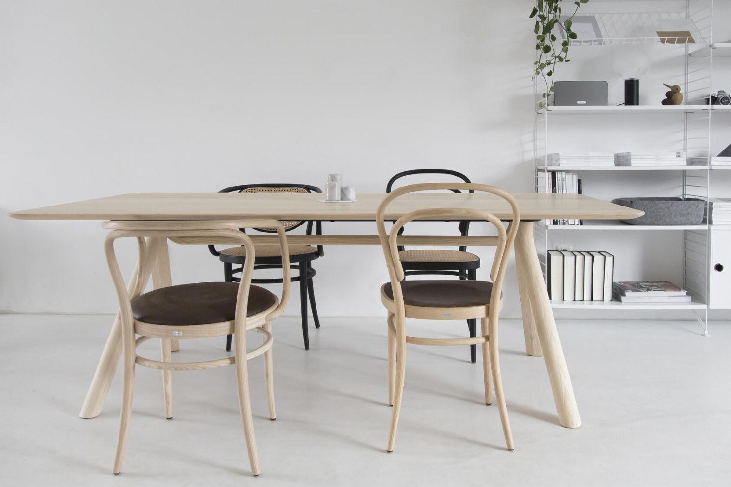 Moderner Essbereich mit hellem Holztisch, schwarzen und naturfarbenen Stühlen, minimalistischem Regal und Pflanzen.