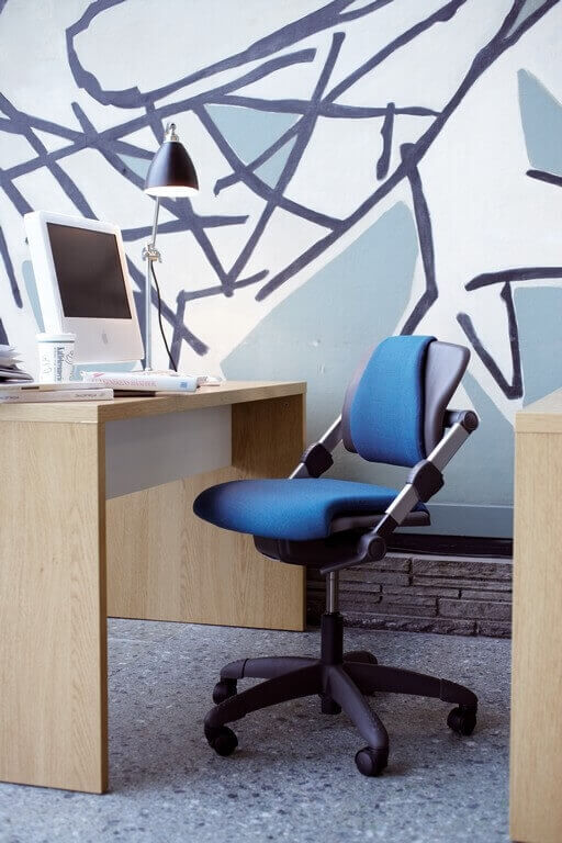 Ergonomischer Bürostuhl in Blau vor einem Schreibtisch mit Computer und Designerlampe, moderner Arbeitsplatz.