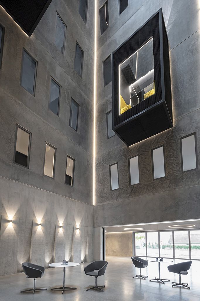 Modernes Atrium mit hohen Decken, minimalistischen Möbeln und einem schwebenden Raum mit gelben Sesseln.