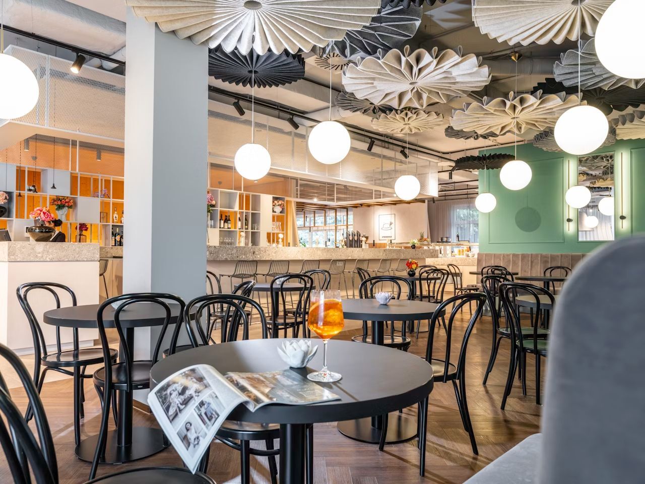 Stylisches Café mit schwarzen Bistrostühlen, modernem Design und Aperitif auf dem Tisch, beleuchtet von Kugelleuchten.