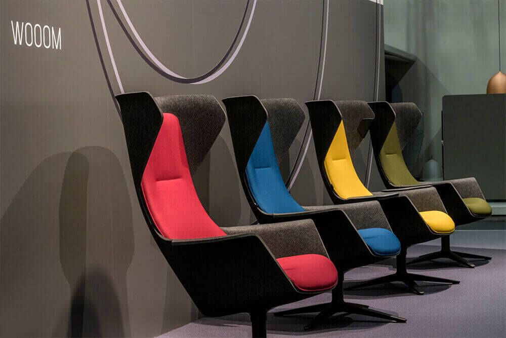 Vier ergonomische Stühle mit bunten Polstern in Rot, Blau, Gelb und Grün in modernem Design ausgestellt.