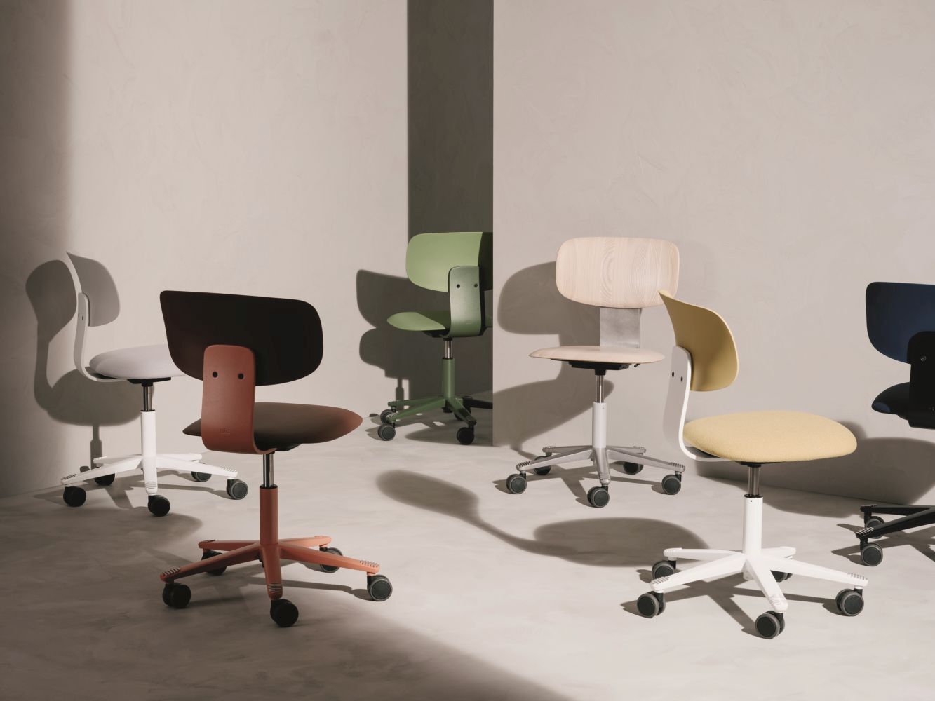 Fünf ergonomische Bürostühle in verschiedenen Farben stehen in einem minimalistischen Raum mit neutralen Wänden.
