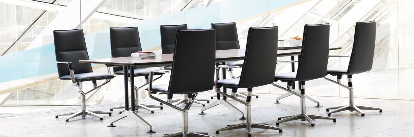 Moderner Konferenztisch mit acht schwarzen ergonomischen Bürostühlen in einem hellen, verglasten Raum.