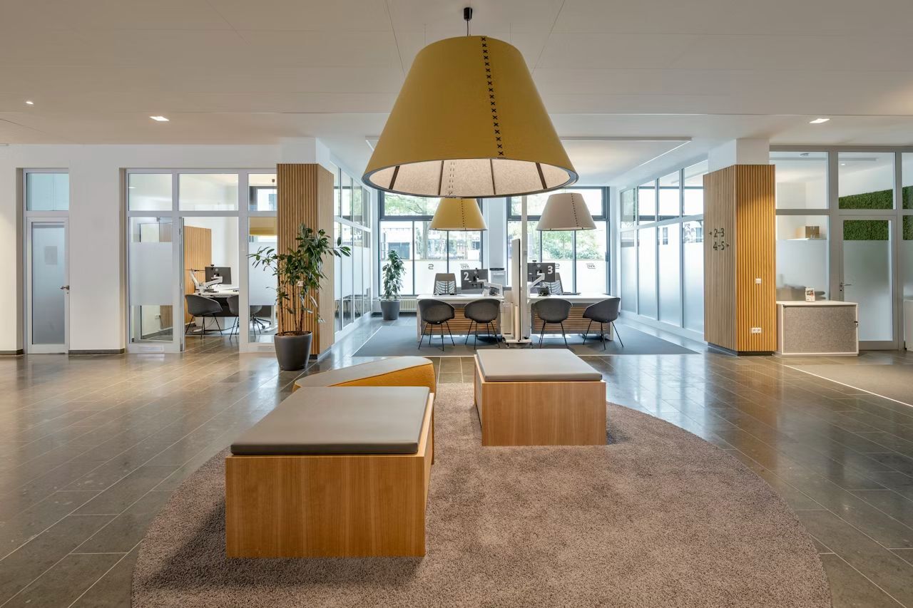 Geräumiger, moderner Empfangsbereich mit Holzmöbeln, großen Lampen und ergonomischen Stühlen für dynamisches Sitzen.